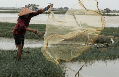 Full length of man casting fishing nets on lake