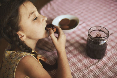 Cute funny toddler girl eats sweet bun  breakfast. happy child eating bread roll with strawberry jam