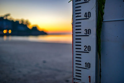 Close-up of information sign on beach against sky during sunset