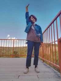 Full length portrait of happy man standing by railing against sky