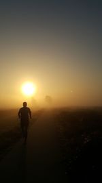 Rear view of silhouette man walking on landscape against sunset sky