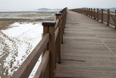 Wooden railing on beach against sky