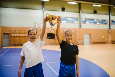 Portrait of happy female players holding trophy while standing together in sports court