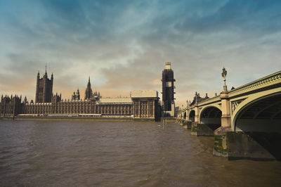 Bridge over river in city against cloudy sky