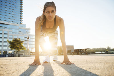 Determined young woman exercising on footpath against building during sunny day in city