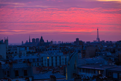 Distant view of eiffel tower in city against cloudy dramatic sky during sunset