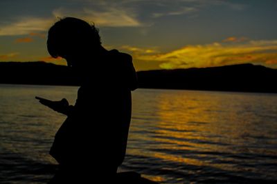 Silhouette boy standing on beach against sky during sunset