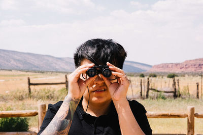 Man looking through binoculars against cloudy sky