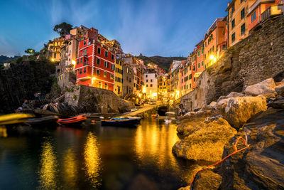 Illuminated buildings by canal against sky at night