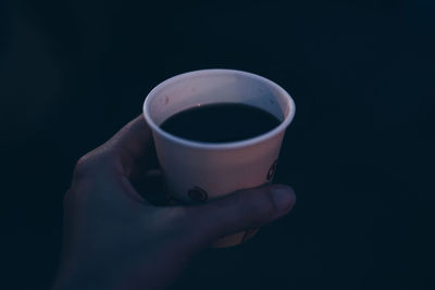 Close-up of hand holding coffee cup against black background