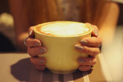 Close-up of hand holding coffee cup on table