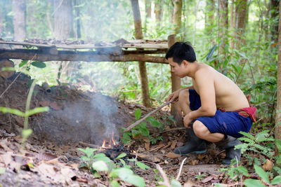 Side view of shirtless man sitting in forest