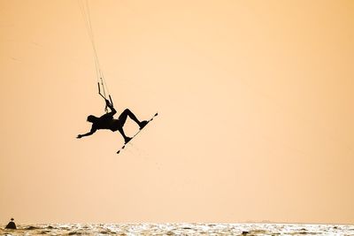 Silhouette man kiteboarding over sea against clear sky during sunset