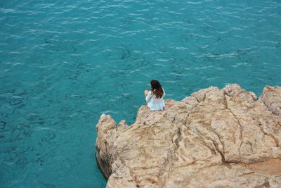 High angle view of woman sitting on rock by sea