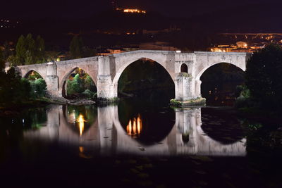 Arch bridge over river by illuminated buildings at night