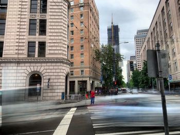 Blurred motion of people walking on road against buildings