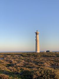 Lighthouse on land by building against clear sky