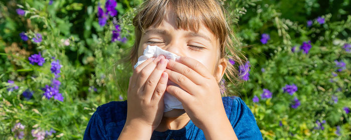 Girl wiping nose with tissue against plants