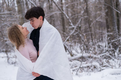 Couple wrapped in blanket embracing outdoors during winter