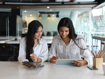 Smiling colleagues using digital tablet sitting in office