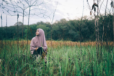 Woman wearing hijab sitting on grassy field