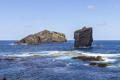 Rocks on shore by sea against sky