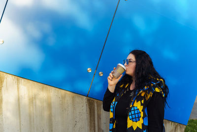 Brunette woman with long curly hair drinks coffee from a paper cup