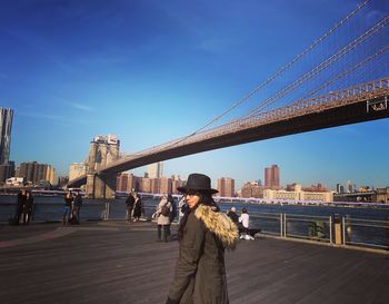 Young woman standing at promenade by brooklyn bridge over east river