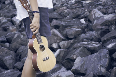 Midsection of man holding guitar on rocks