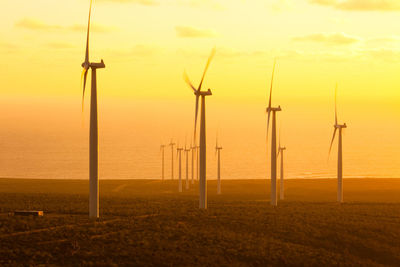 Windmills on field by sea against sky during sunset