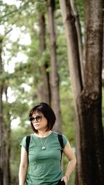 Portrait of woman standing by tree trunk in forest