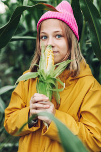 Funny little girl dressed in a yellow raincoat and a hot pink cap spoils and bites corn 