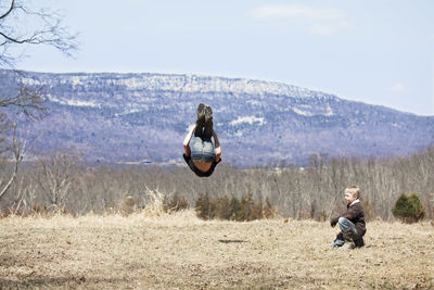 Boy looking at brother performing somersault on field