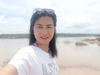 Portrait of woman taking selfie while standing by lake