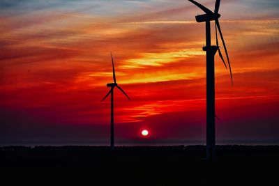 Silhouette wind turbines on field against orange sky