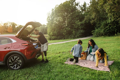 Family preparing for picnic while sitting on grass near car at park