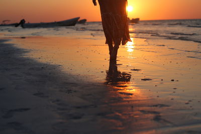 Low section of woman walking on shore at beach during sunset