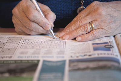 Cropped hand of senior woman writing on newspaper