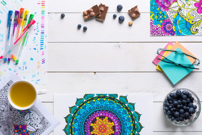 High angle view of blueberries with coffee and plant by art and craft equipment on table