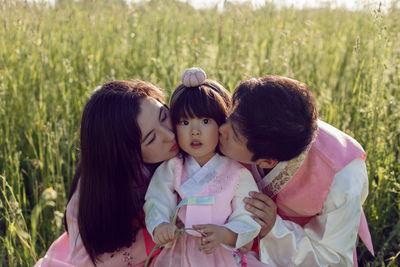 Korean family in national costumes is sitting in a field at sunset in the grass 