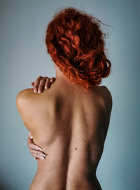 Rear view of shirtless woman standing against gray background