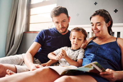 Father and mother reading book with son on bed