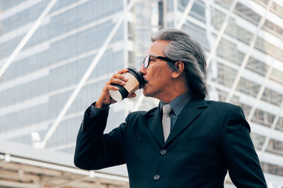 Businessman drinking coffee against office building