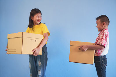 Smiling boy and girl holding shopping bags and container against colored background