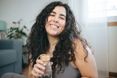 Portrait of young woman holding water bottle at home