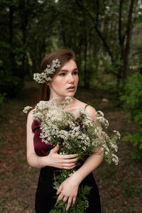 Young woman holding flowers against trees in park