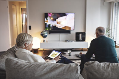 Senior woman using digital tablet while partner sitting on sofa in living room