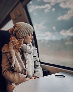 Young woman looking away while sitting in car window