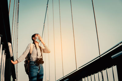 Low angle view of person standing by railing against sky