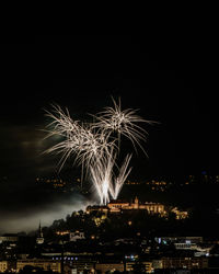 Firework display in city against sky at night